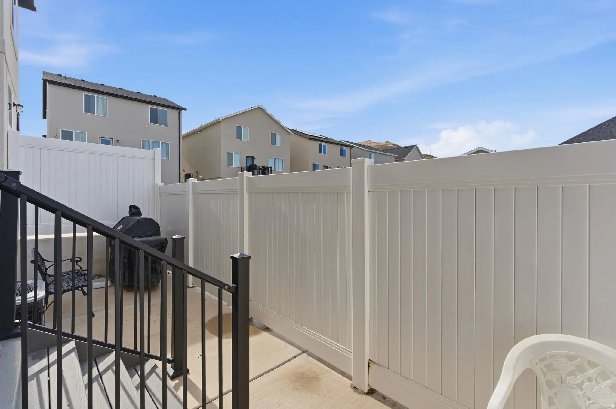 Private outdoor patio space featuring concrete flooring, white vinyl fencing, and black metal railings