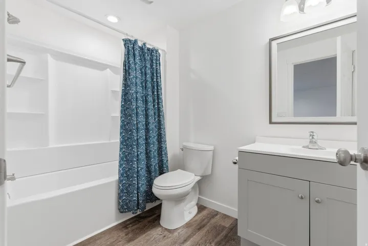 Bathroom featuring a white tub/shower combination with built-in shelving, a modern toilet, a gray vanity with a white countertop, and a framed mirror