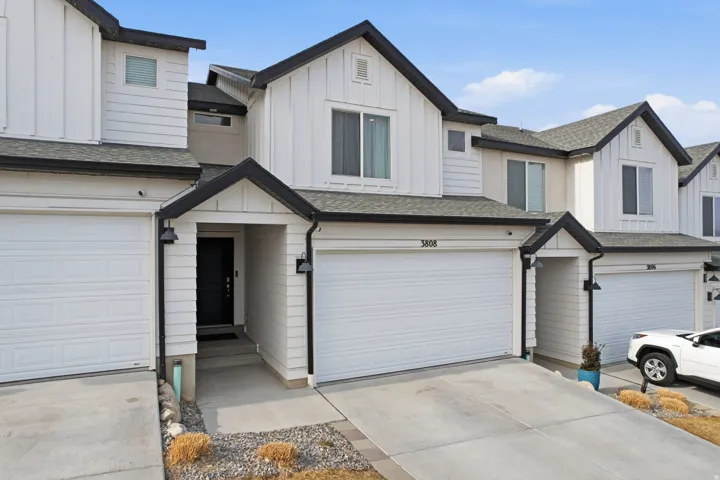 Modern townhome exterior featuring white vertical and horizontal siding, a prominent attached garage, and a covered entry with a dark door