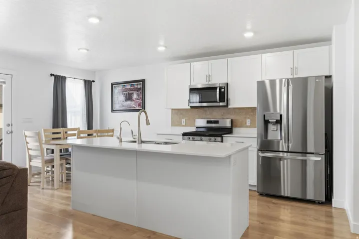 Contemporary kitchen featuring white cabinetry, stainless steel appliances, a center island with sink, wood-finish flooring, and recessed lighting