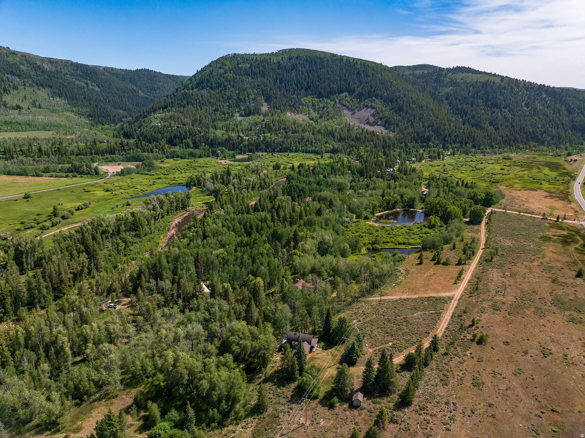 Expansive natural landscape featuring dense tree coverage, a meandering river, and multiple ponds