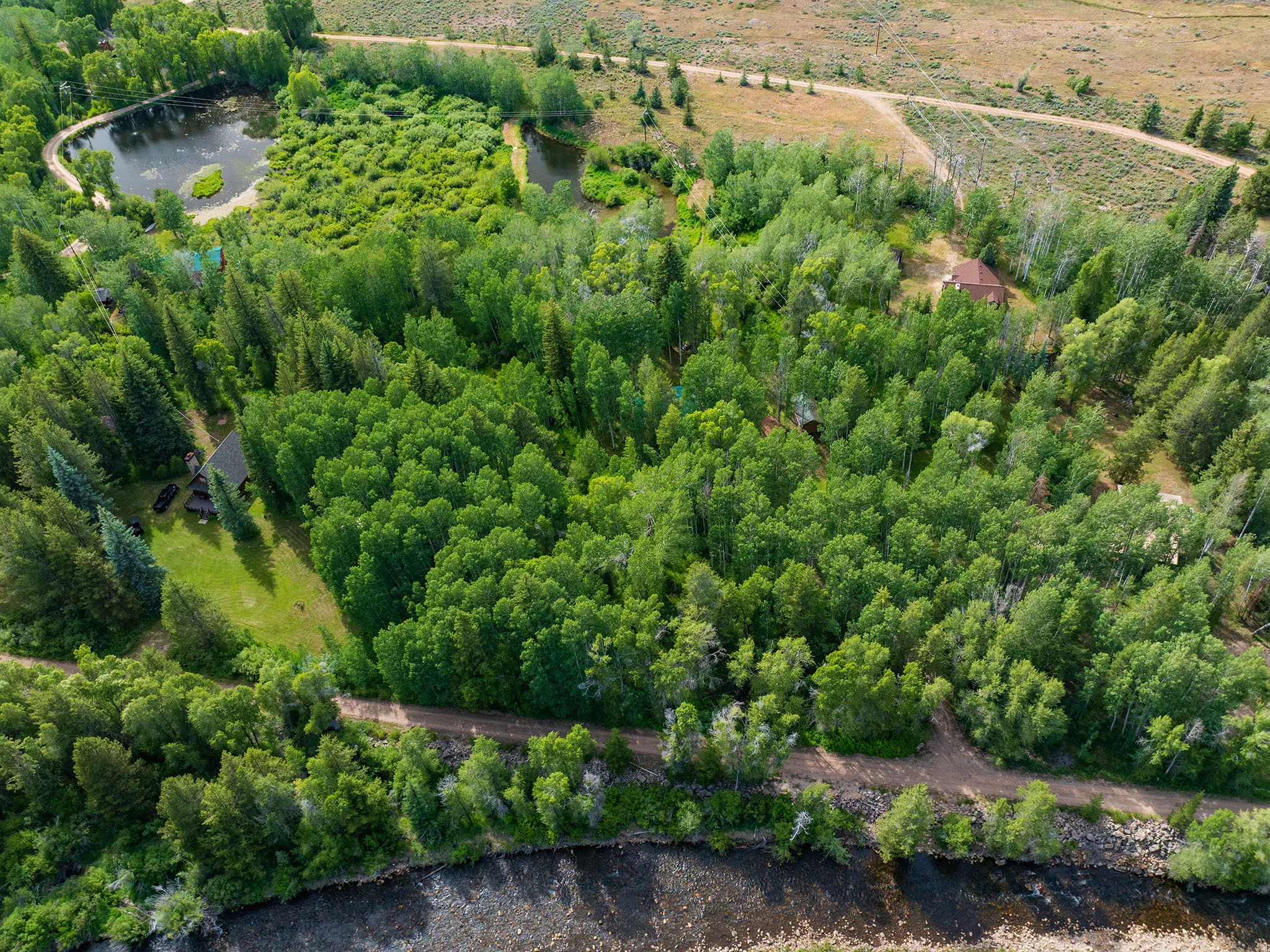 Expansive property featuring dense tree coverage, a large pond, a meandering stream, a river frontage, and multiple structures