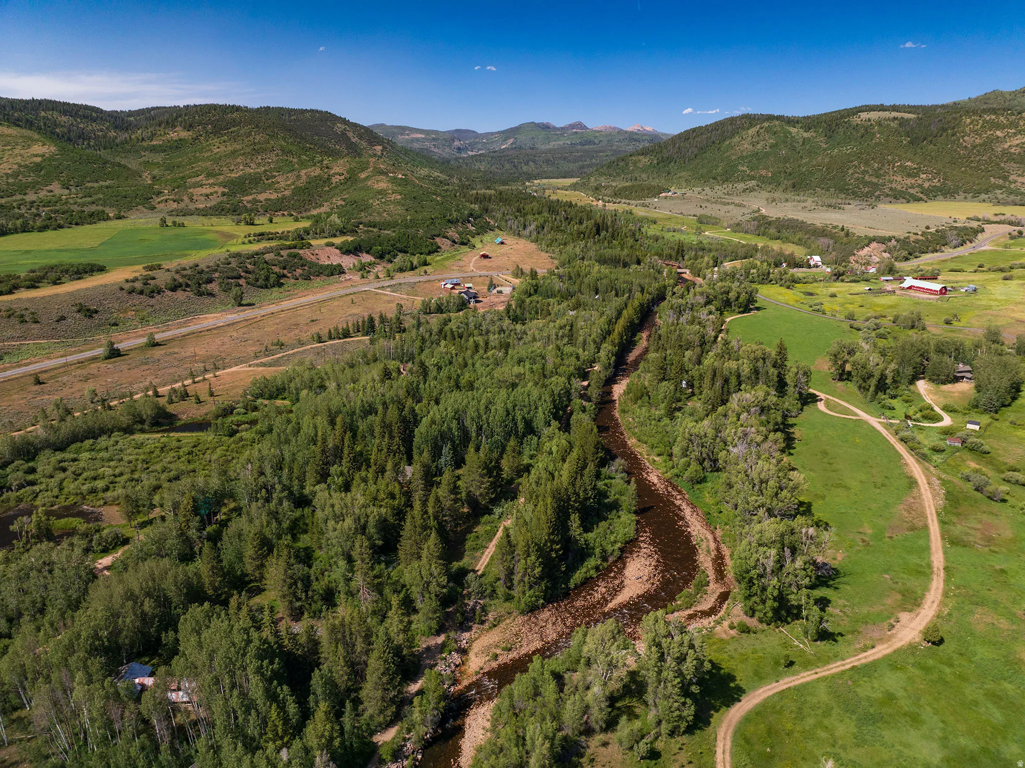 Expansive mountain landscape featuring a winding river, dense tree lines, and open fields