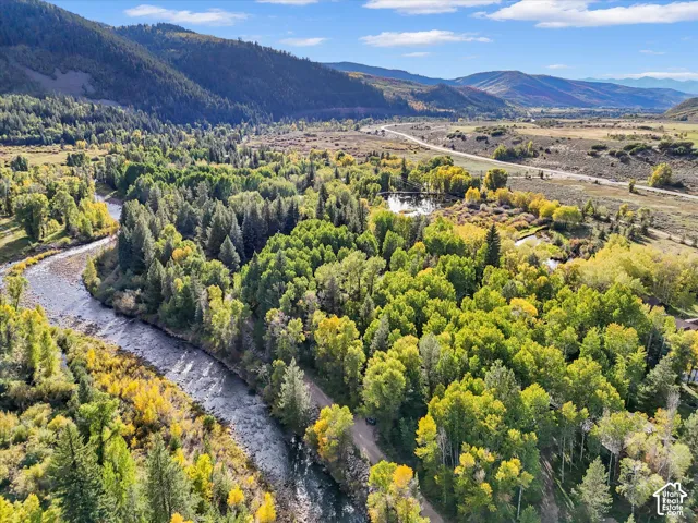 Expansive natural landscape with a winding river, dense tree cover, distant mountains, and a secluded pond