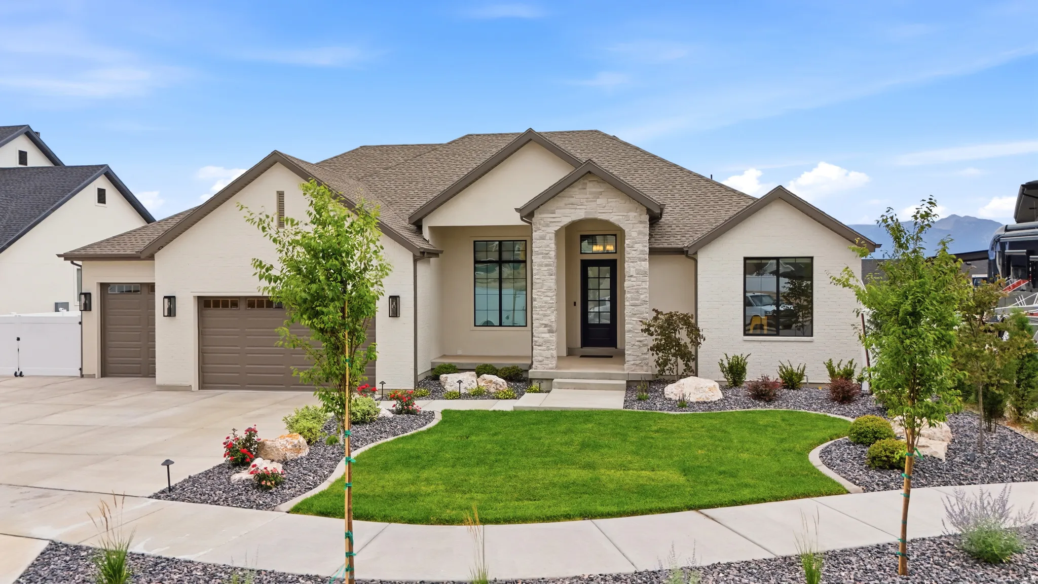 Contemporary stucco exterior with a stone accent entry, dark trim windows, and two garage bays