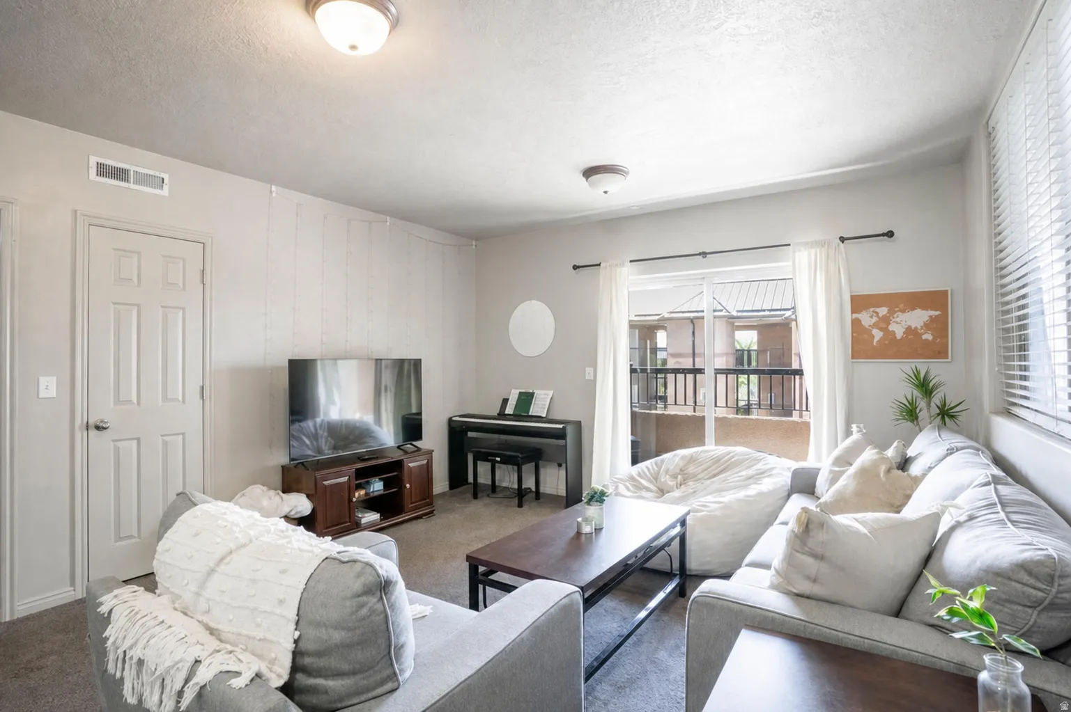 Living area featuring neutral wall tones, carpeted flooring, a ceiling-mounted light fixture, and a sliding glass door providing exterior access