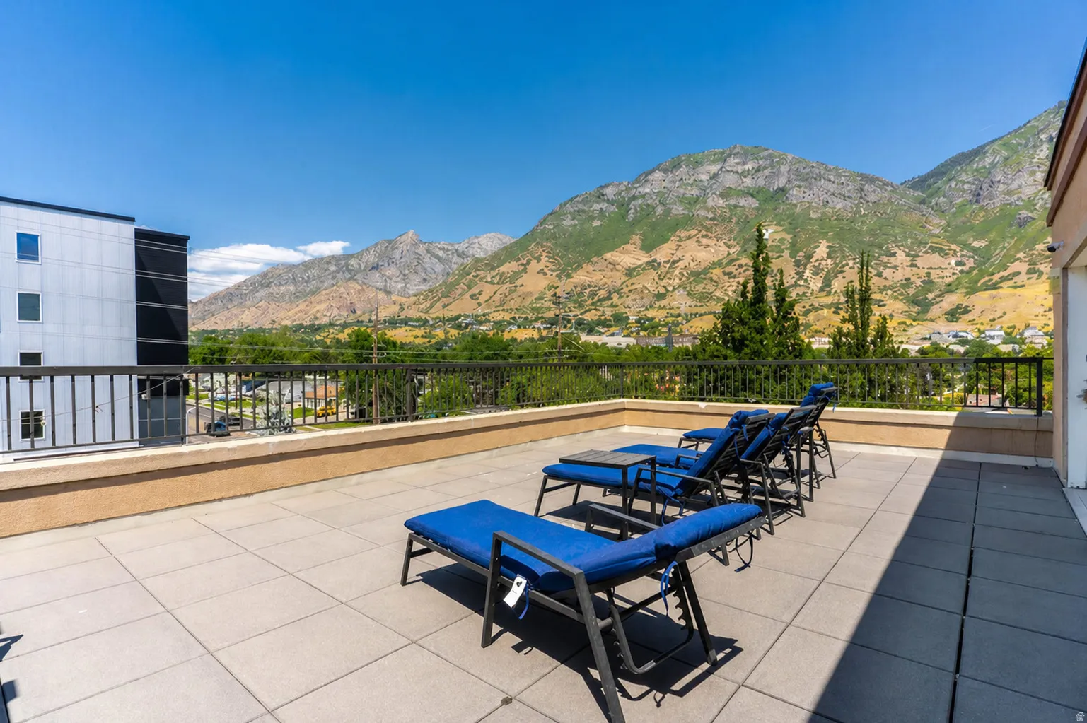 Rooftop patio with large format tile flooring, stucco wall, and metal railing