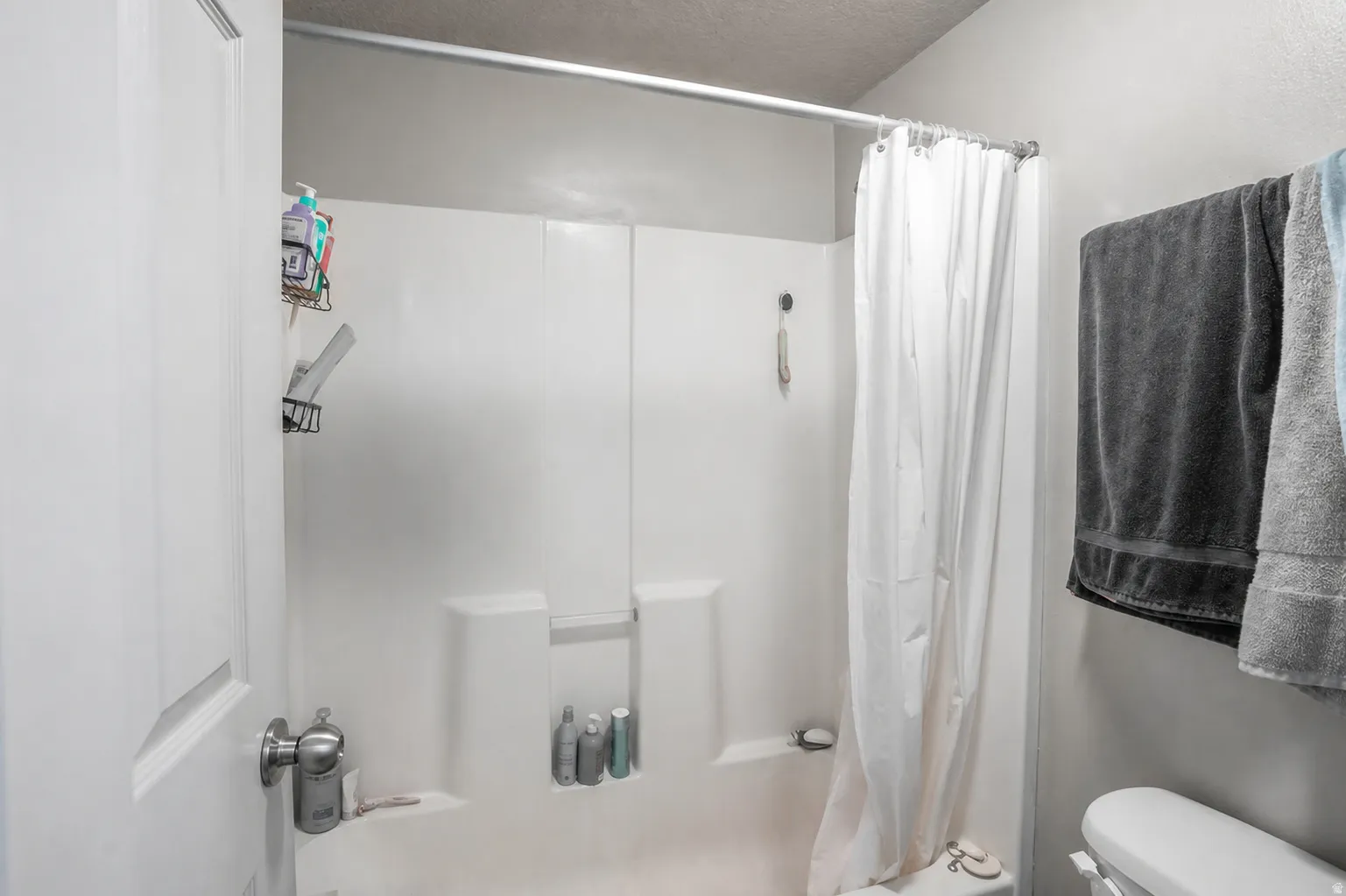 White fiberglass shower-tub combination featuring a built-in shelf and showerhead with hose