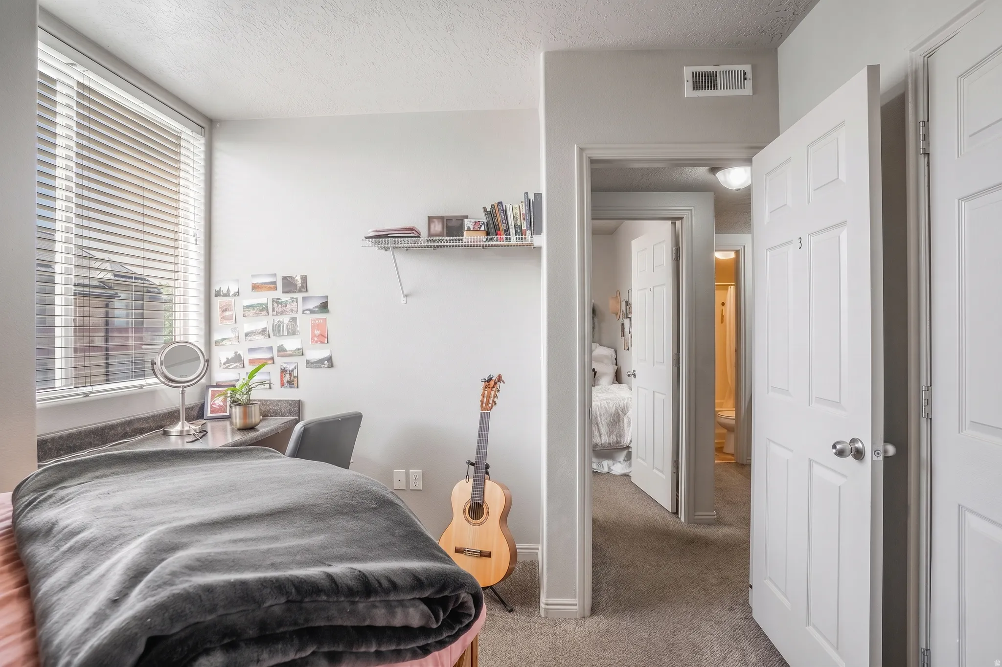 Room featuring a large window with horizontal blinds, built-in desk with a dark countertop, light gray walls, and light-colored carpeting