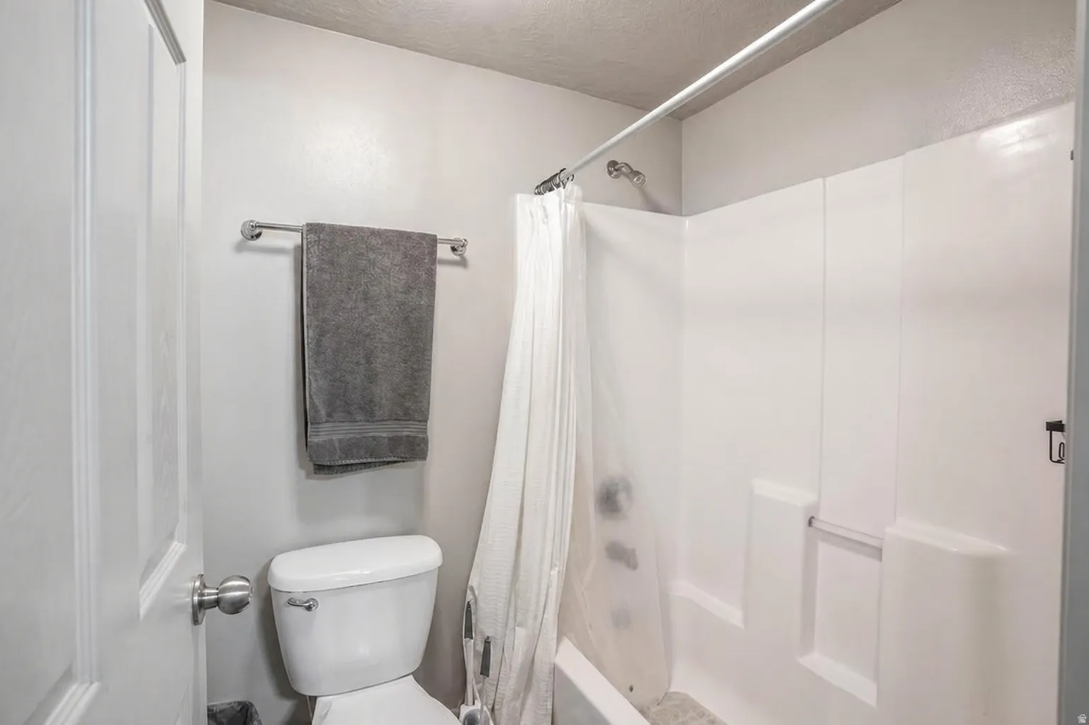 Full bathroom featuring a white toilet, chrome towel bar, and a shower-tub combination with a white surround