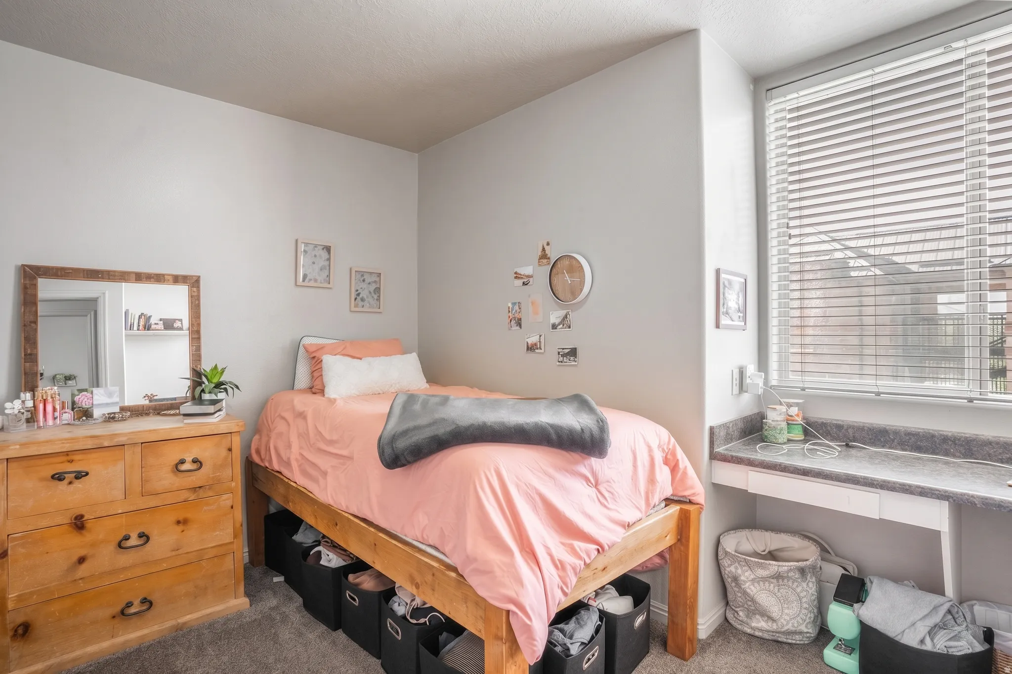 Carpeted room featuring light gray walls, a built-in desk with a dark countertop, and a window with horizontal blinds