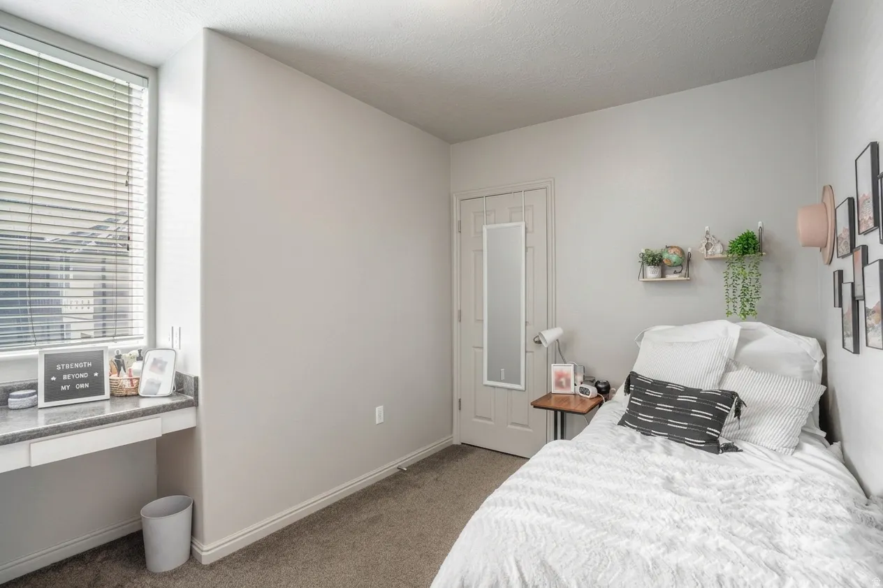 Bedroom featuring neutral wall paint, carpet flooring, a window with blinds, and built-in desk with a stone-finish countertop
