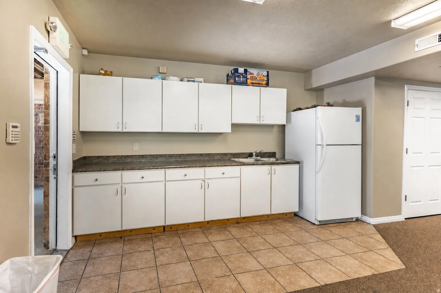 Functional kitchenette featuring white cabinetry, a single basin sink, and a refrigerator