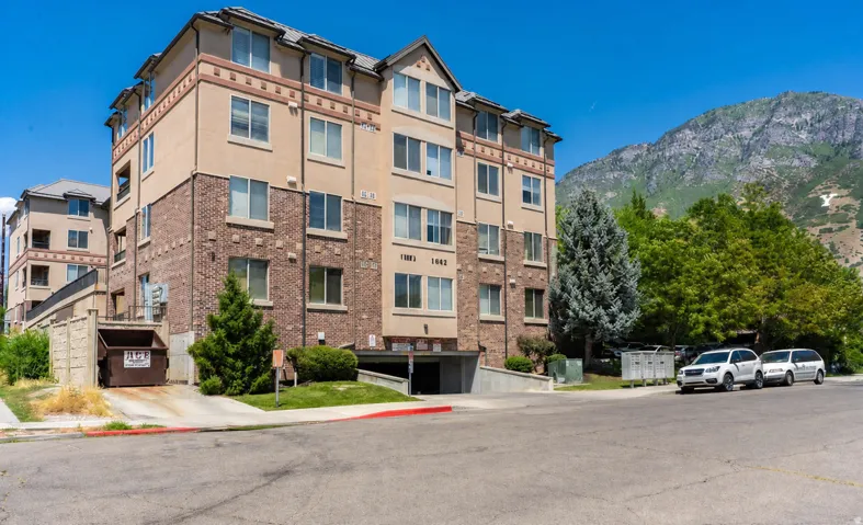 Multi-story building featuring brick and stucco facade, an integrated parking garage entrance, and a mountain backdrop