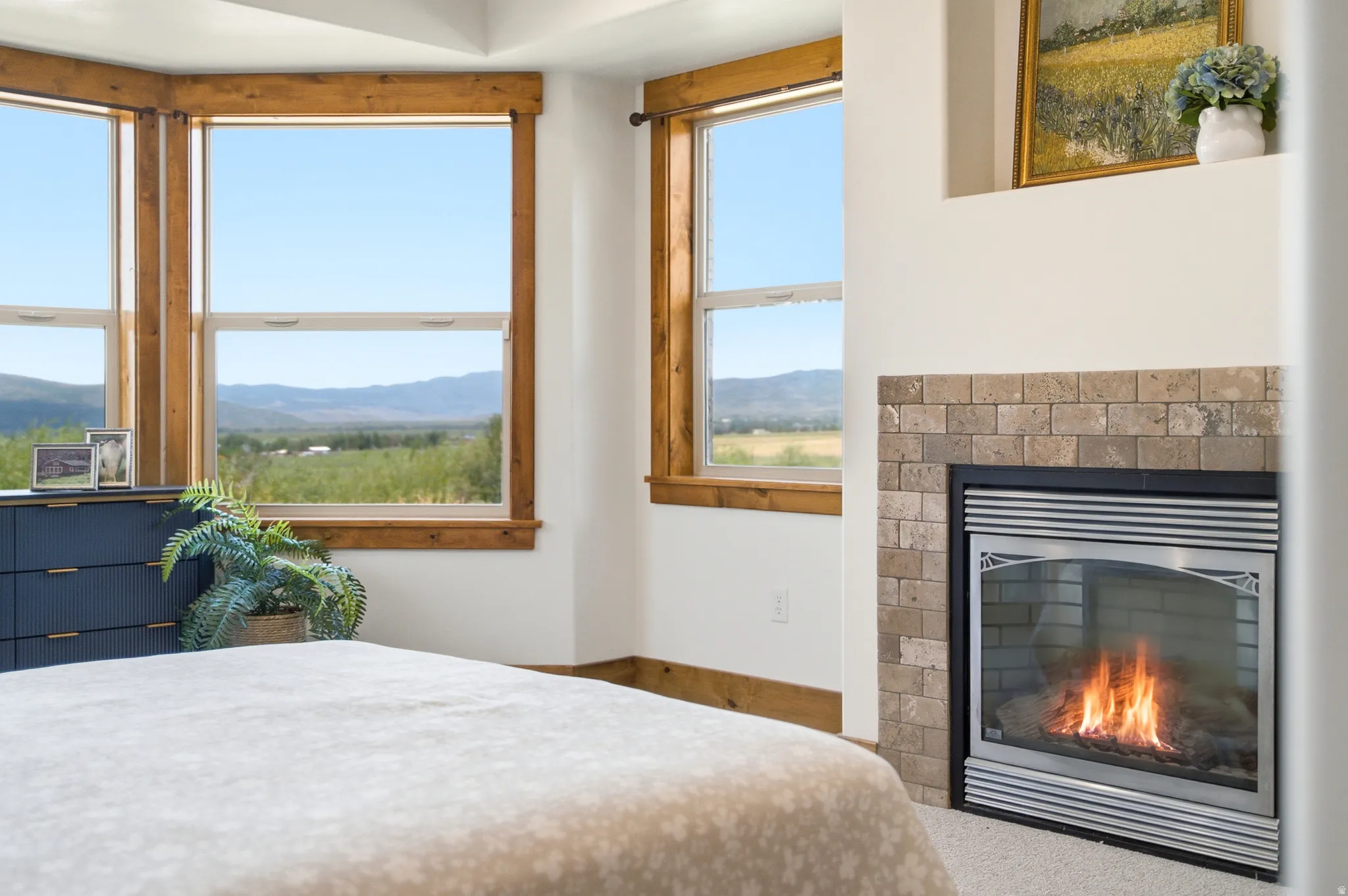 Built-in fireplace with a stone-tile surround, multiple large windows with wood trim, and a tray ceiling