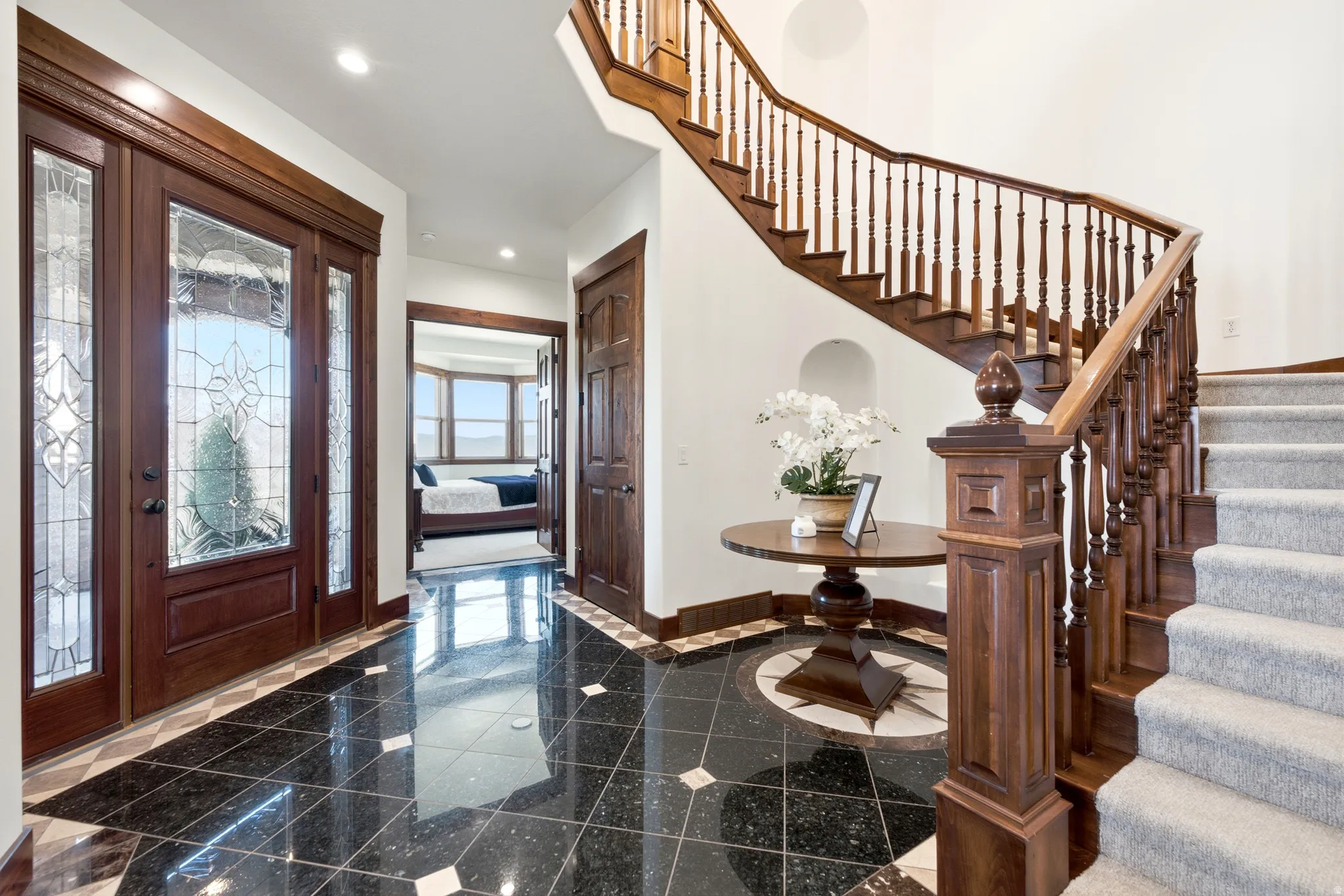 Grand entry featuring a dark wood staircase with ornate balusters, black tile flooring, and a decorative tile inlay