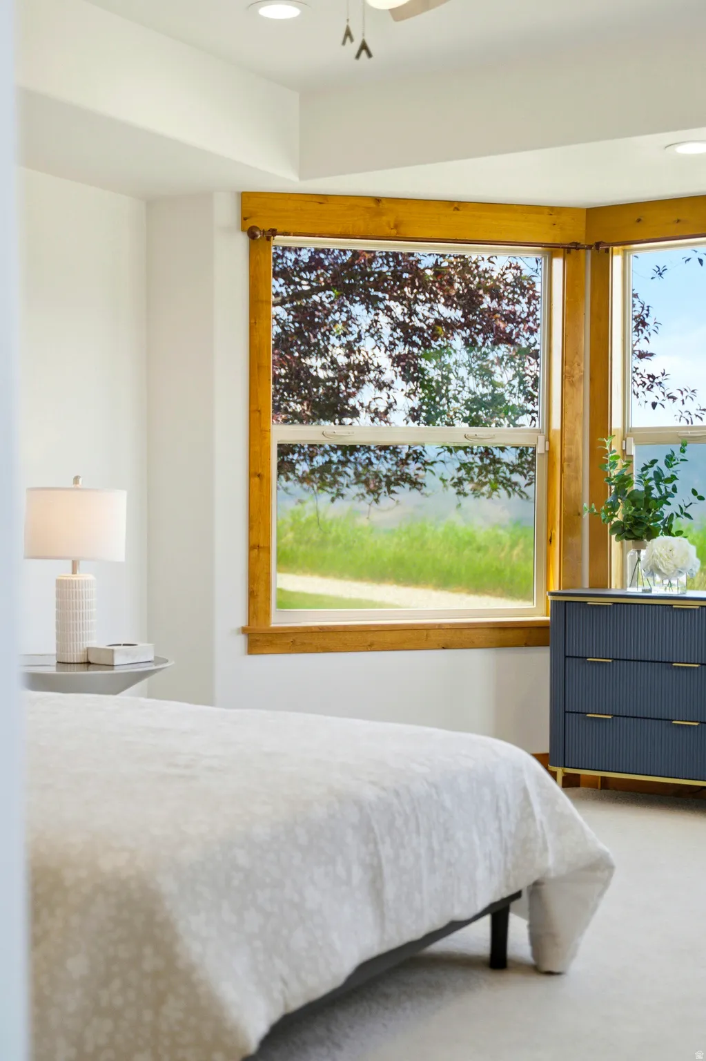 Bay window with natural wood trim, recessed lighting, ceiling fan, and light-colored carpet flooring