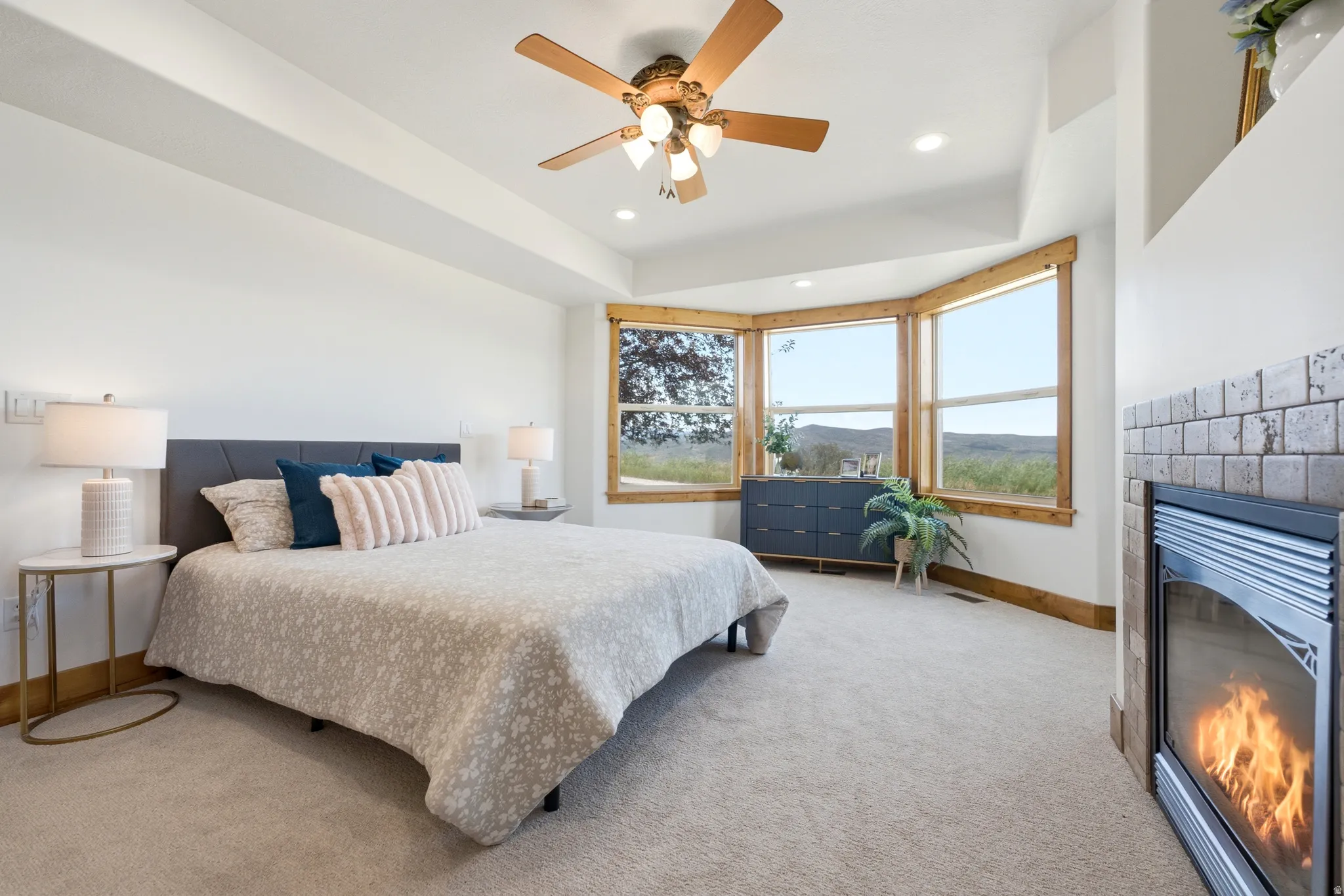 Bedroom featuring a multi-pane bay window with natural wood trim, a ceiling fan with integrated lighting, recessed lighting, and a built-in fireplace with a tiled surround