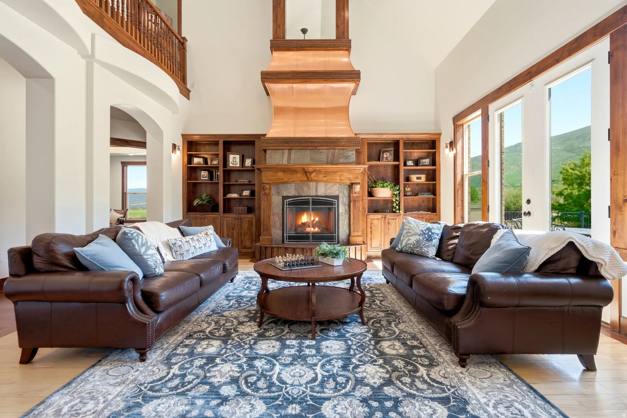 Spacious living area featuring a prominent stone fireplace with a wood mantel, built-in shelving, and light wood-finish flooring