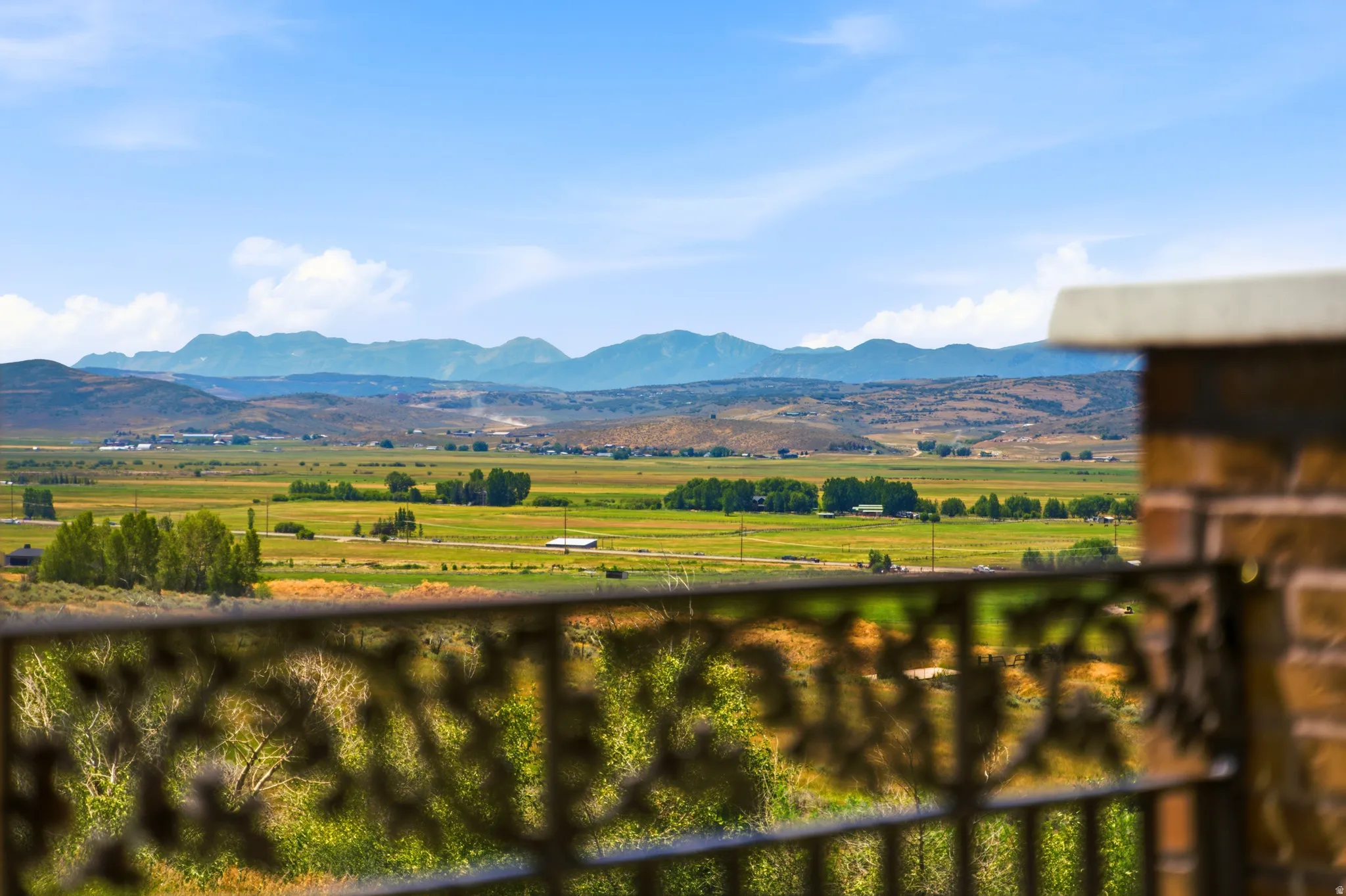 Expansive pastoral landscape featuring distant mountains and a decorative wrought iron railing