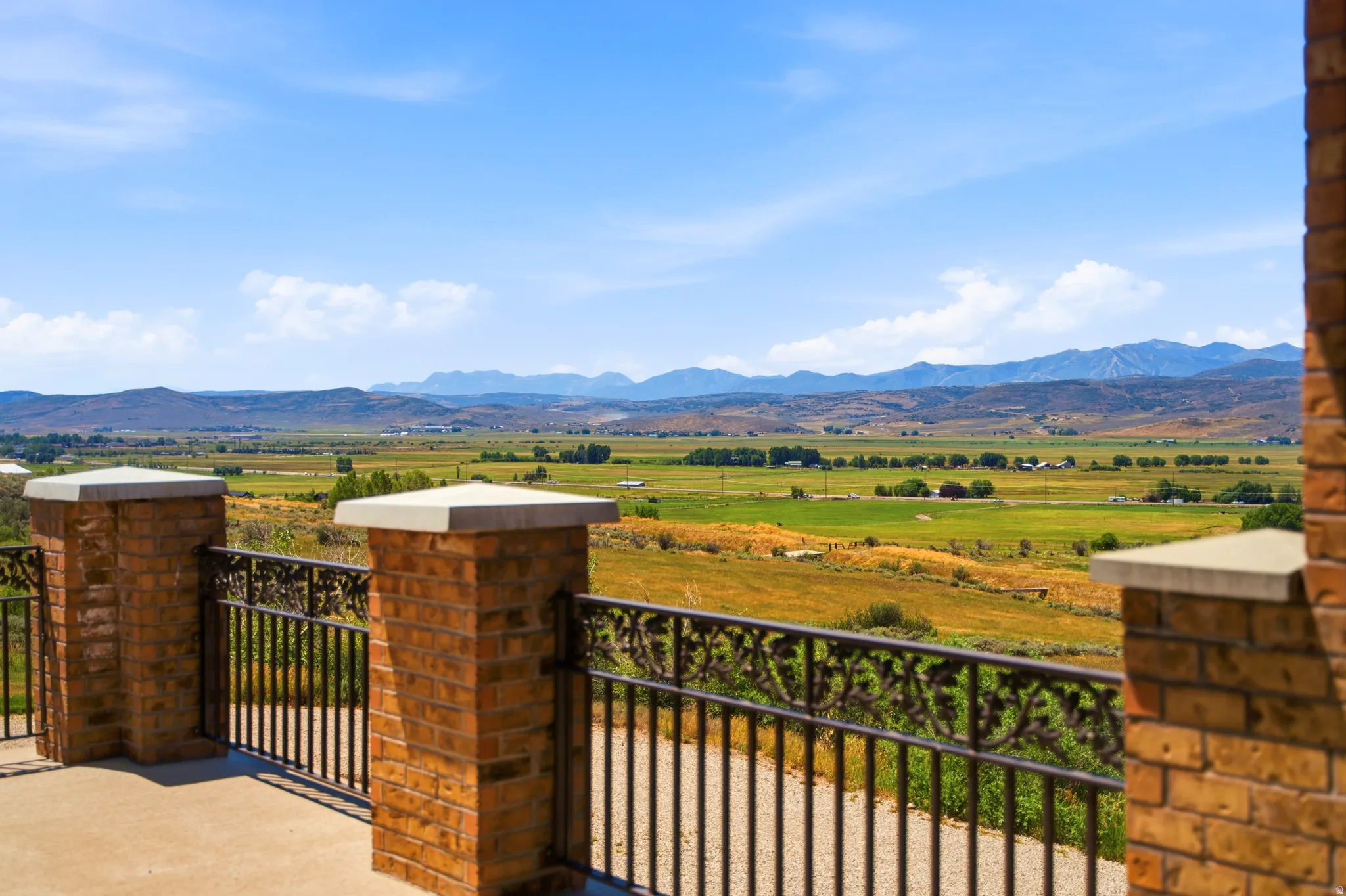 Exterior balcony featuring brick pillars with capstones and decorative metal railing, overlooking expansive green fields and distant mountains