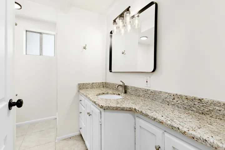 Bathroom vanity featuring a speckled countertop, undermount sink, and a framed mirror with an attached multi-bulb light fixture