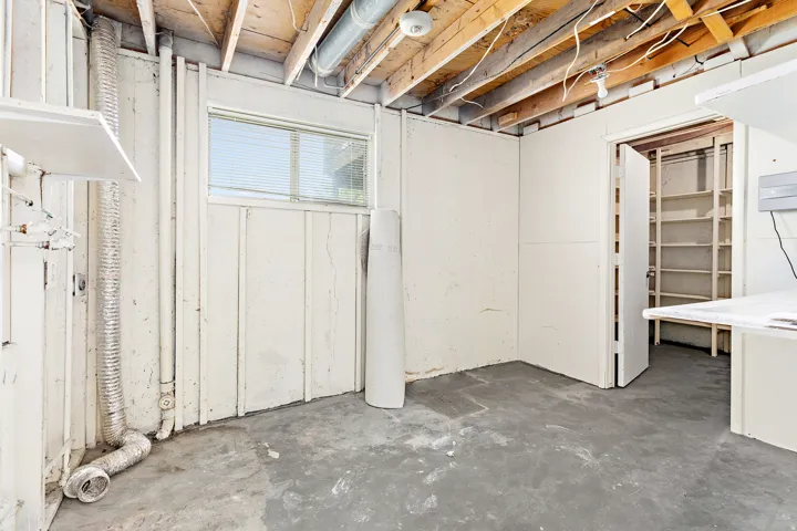 Unfinished basement area featuring exposed ceiling joists, concrete flooring, and a single window with blinds