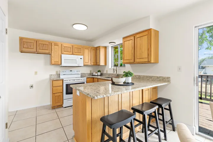 Kitchen featuring wood cabinetry, granite-finish countertops, white appliances, a breakfast bar, and tile flooring
