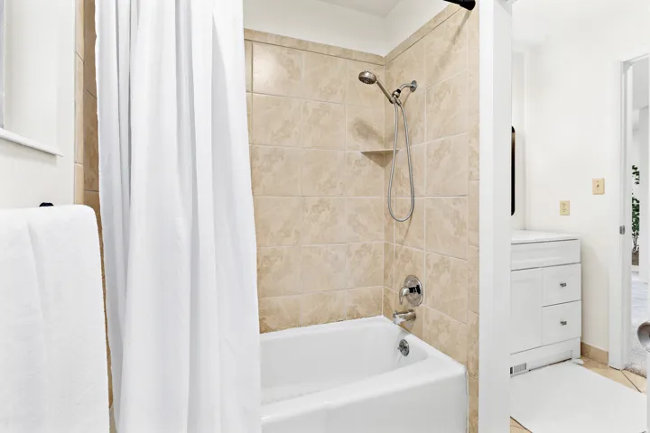 Bathtub with tiled surround featuring a built-in shelf and chrome fixtures