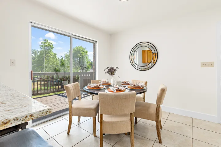 Dining area featuring a sliding glass door, neutral-toned tile flooring, light-colored walls, and a round wall mirror