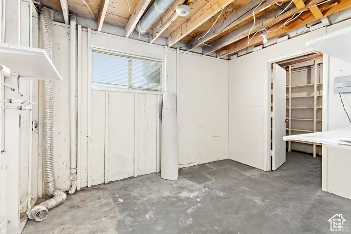 Unfinished basement area featuring exposed ceiling joists, concrete flooring, and a single window with blinds