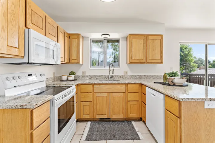 U-shaped kitchen featuring wood cabinetry, granite-finish countertops, white appliances, and a stainless steel sink with a gooseneck faucet
