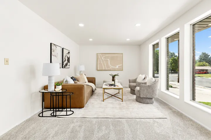 Spacious living area featuring light-toned carpeting, ample natural illumination from multiple tall windows, recessed ceiling lighting, and crisp white wall finishes