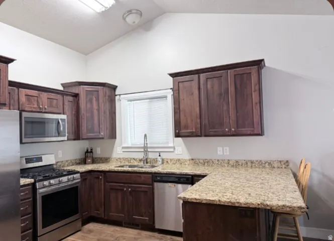 Kitchen featuring vaulted ceilings, wood-finish flooring, dark wood cabinetry, granite countertops and bar with  barstools.