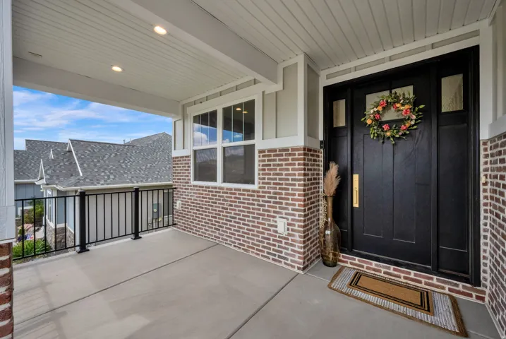 Covered front porch featuring a dark paneled entry door, transom windows, and brick facade