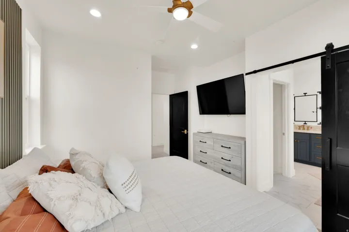 Contemporary bedroom space featuring a ceiling fan with integrated lighting, recessed lighting, and a barn door entry to a bathroom