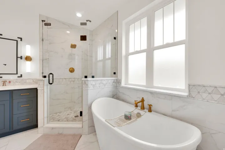 Freestanding soaking tub with gold-finish fixtures and a large window featuring privacy glass