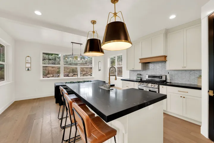 Gourmet kitchen featuring a large island with dark countertops, white shaker cabinetry, stainless steel range, light wood-finish flooring, and multiple windows