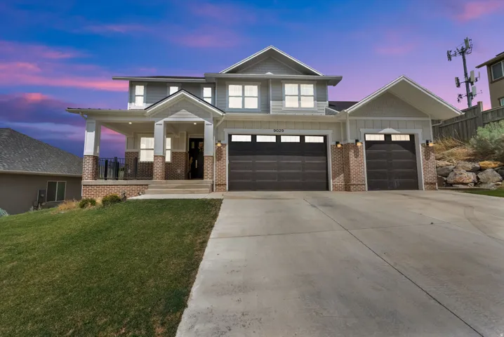 Two-story residence featuring a covered front porch with dark railings and brick accents, a two-car garage with individual doors, and a separate single-car garage