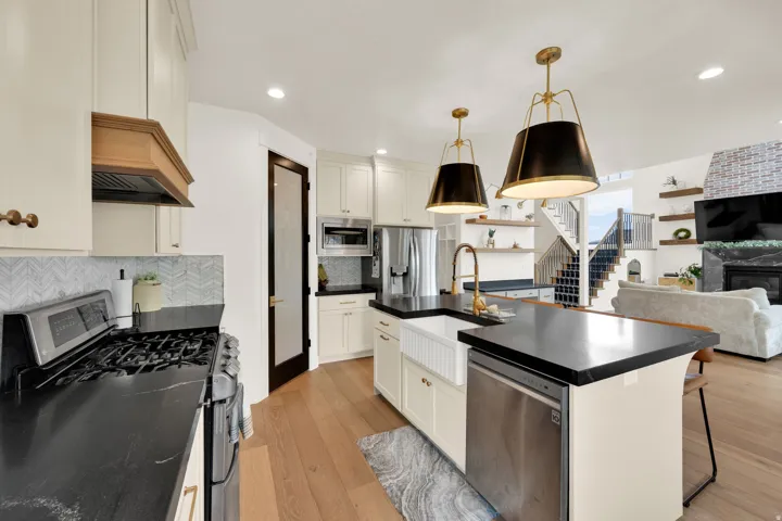 Open-concept kitchen featuring white cabinetry, dark countertops, a large farmhouse sink, and two pendant lights