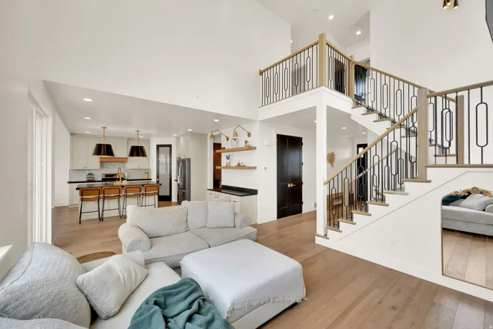 Spacious interior featuring a grand staircase with decorative metal balusters and wood-finish handrails, high ceilings, light wood-finish flooring, a kitchen with an island and pendant lighting, and a built-in wet bar with open shelving