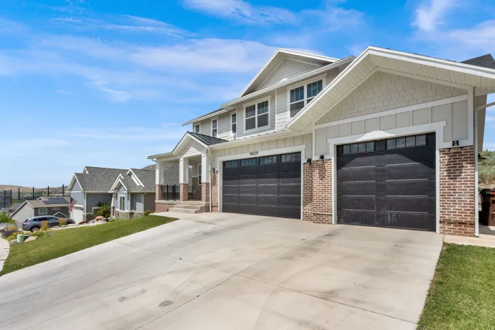 Multi-level residence featuring a two-car garage with black paneled doors, light brick accents, and a covered porch entry