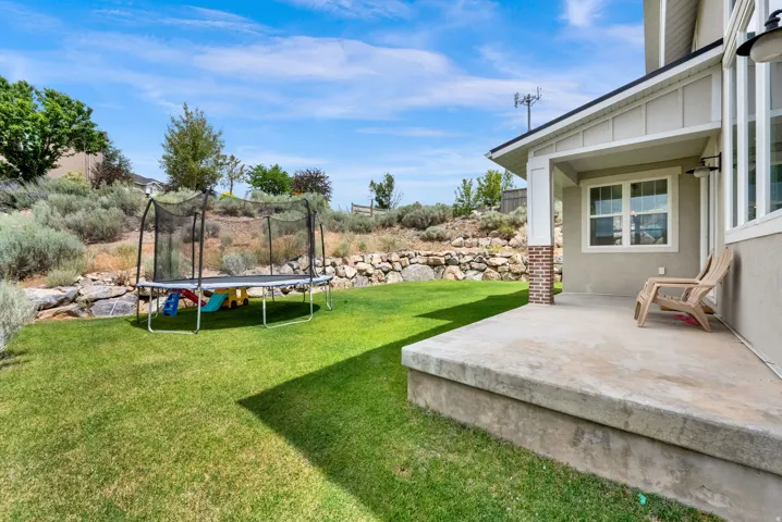 Expansive backyard featuring a manicured lawn, a concrete patio, and a stone retaining wall