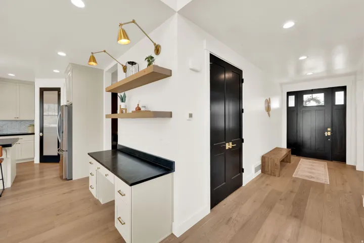 Spacious entryway featuring a dark wood front door with sidelight windows, light wood-finish flooring, and a built-in desk with overhead shelving