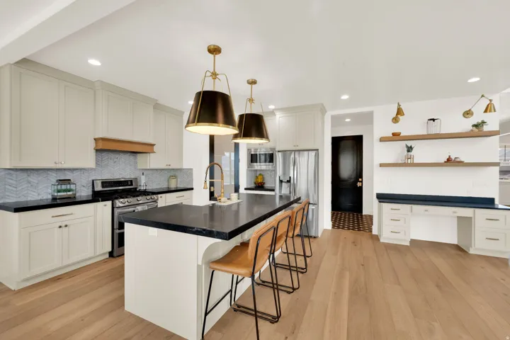 Open-concept kitchen featuring light-toned cabinetry, dark countertops, and a herringbone tile backsplash