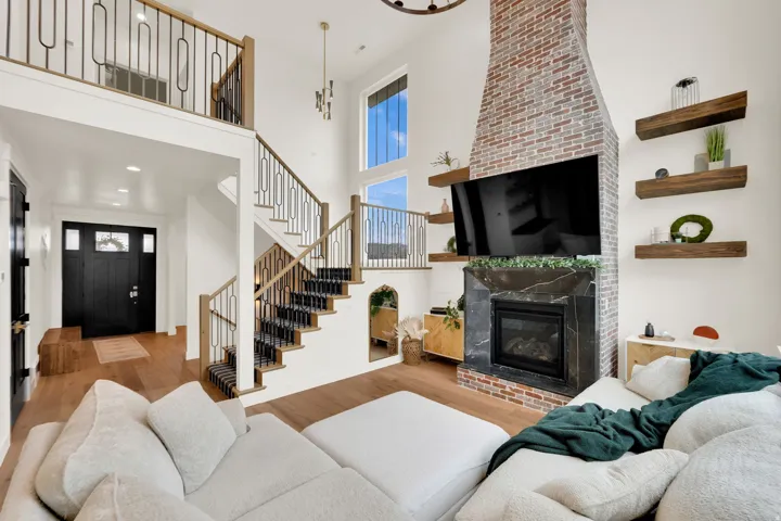 Two-story living area with wood-finish flooring, a brick fireplace with a stone surround, and a staircase featuring wood handrails and black metal spindles
