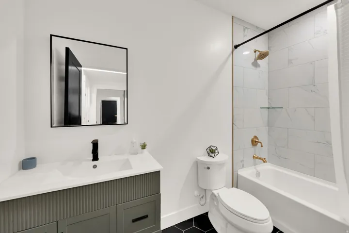 Full bathroom featuring a rectangular soaking tub with white marble-style tile surround and gold-finish fixtures