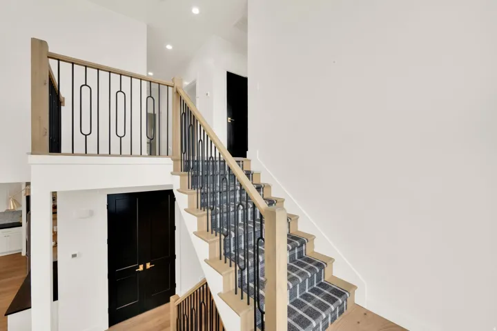Multi-level entryway featuring a natural wood-finish staircase with a plaid runner, iron balusters, and recessed lighting