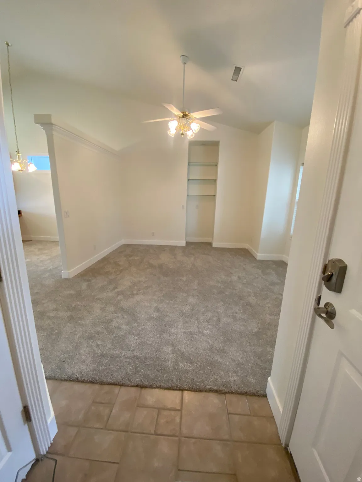 Vaulted ceiling, ceiling fan with light fixture, built-in shelving, carpeted flooring, and tiled entryway