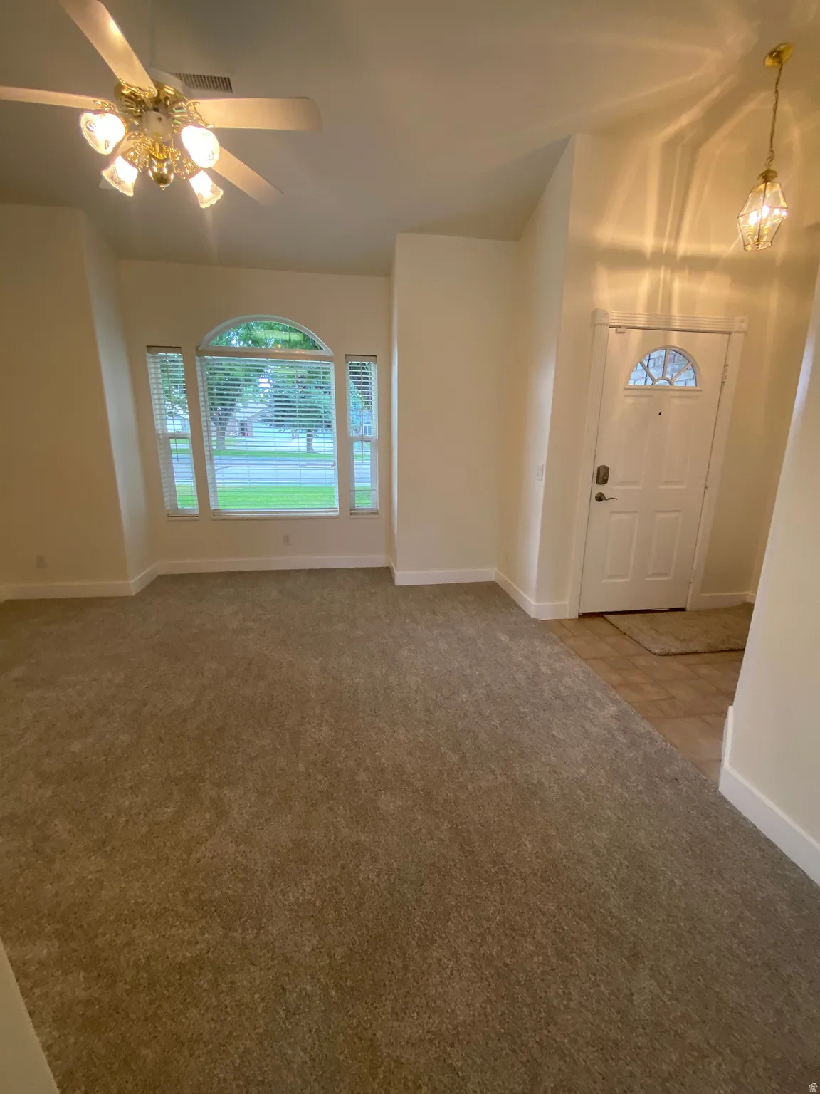 Recessed arched window, window blinds, ceiling fan with integrated lighting, tiled entry, carpeted flooring